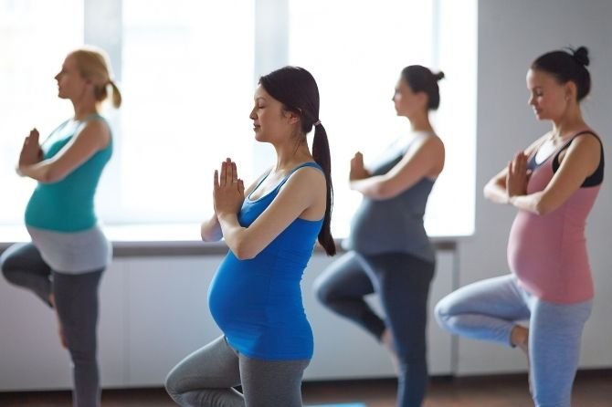 Quatre femmes enceinte dans un cours de Yoga Prénatal collectif, faisant l'asana Vrikshasana