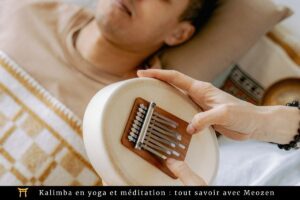 Une personne est allongée sur un lit avec une couverture, tandis qu'une autre main joue du kalimba, un petit instrument de musique, sur sa poitrine. Les deux sont dans une ambiance détendue. Le texte en bas de la page indique : « Kalimba en yoga et méditation : tout savoir avec Meozen.