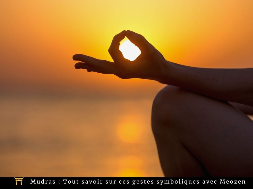 Silhouette d'une main formant un cercle avec ses doigts, positionnée sur un coucher de soleil. Le soleil est visible à travers le cercle formé par les doigts. Le texte en bas indique : « Mudras : Tout savoir sur ces gestes symboliques avec Meozen. ».